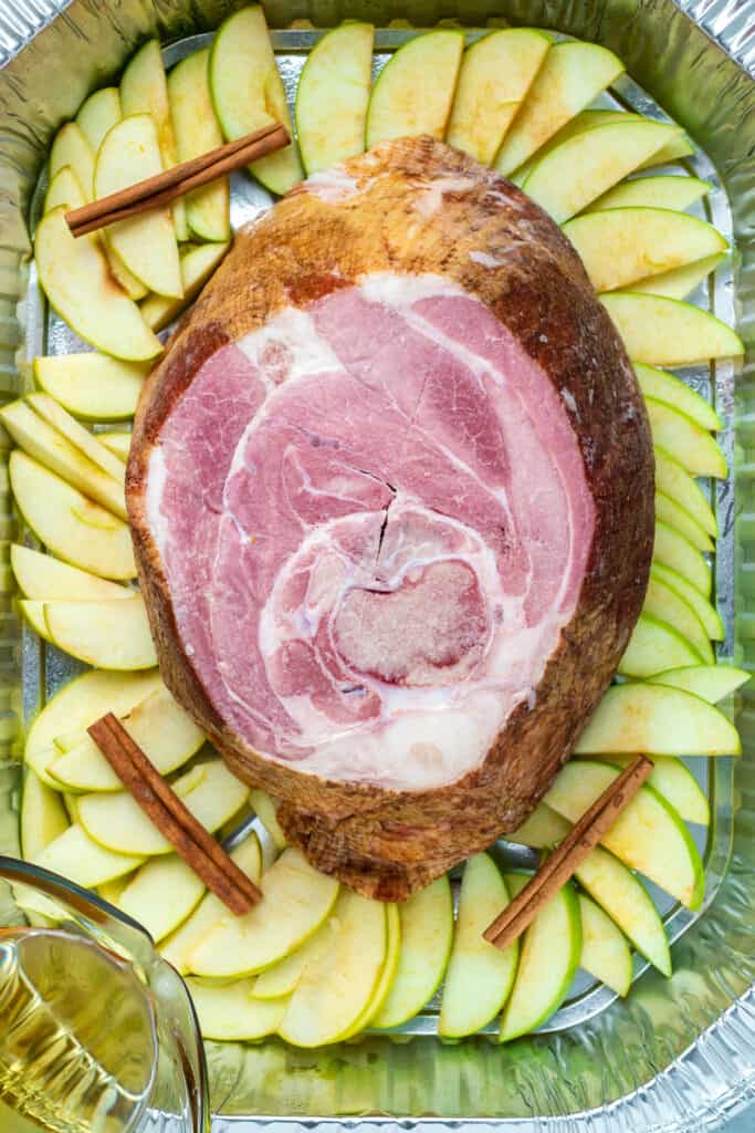 Overhead Image of ham with cinnamon sticks and sliced apples in disposable roasting pan