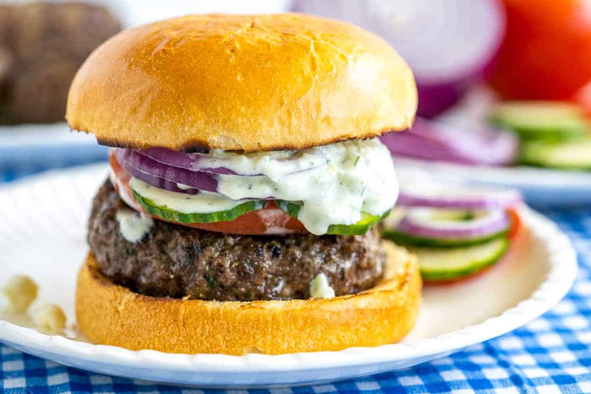 Greek Burger with Tzatziki Sauce on bun on paper plate