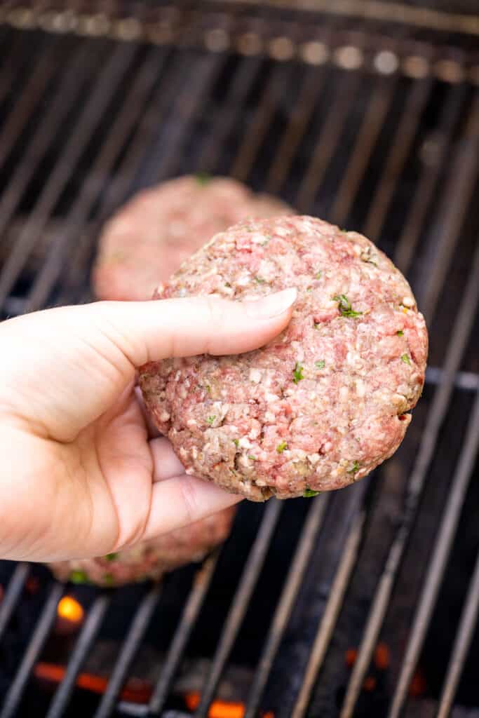 Hand placing burger patty on grill grates