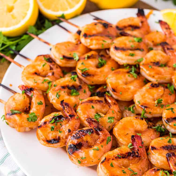 White plate with spicy grilled shrimp skewers on it
