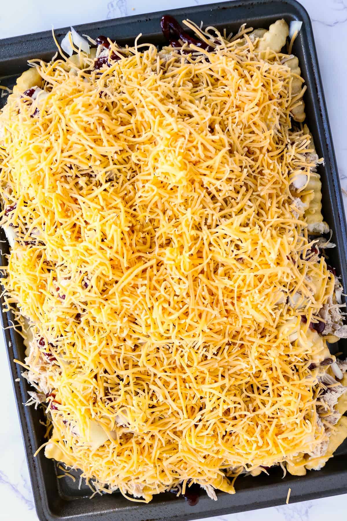 Sheet pan with frozen french fries, pulled pork, BBQ sauce, cheese and onions on it
