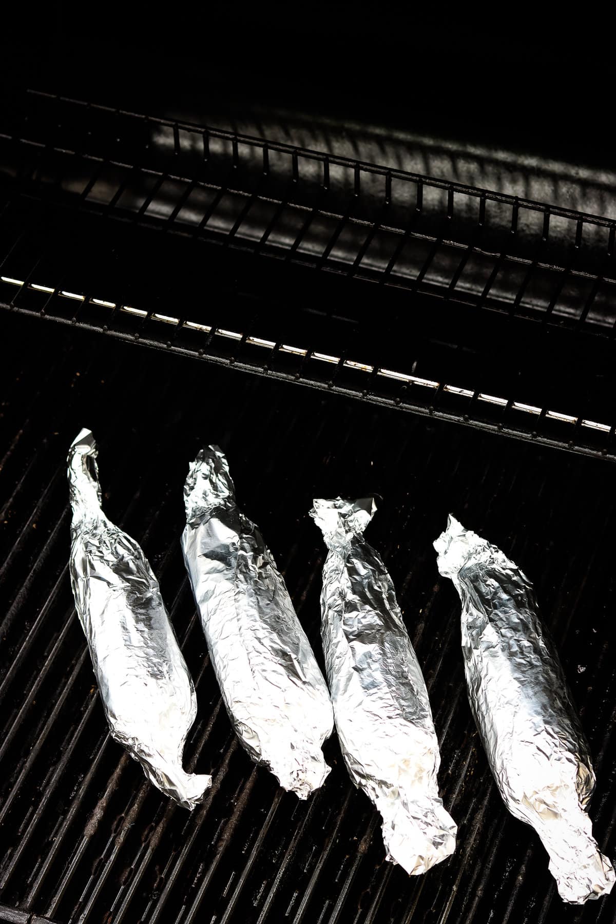 Corn on the cob pieces wrapped in foil on grill grates