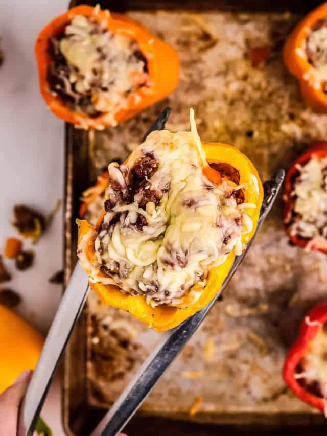 Smoked Stuffed Peppers in between a thong on top of a pan of smoked stuffed peppers
