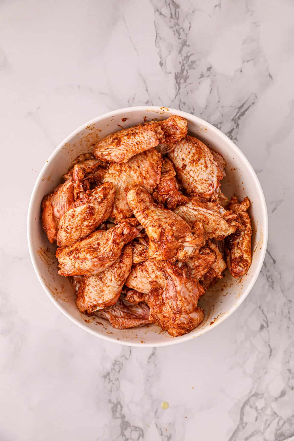 Tossing Chicken Wings with Olive Oil and BBQ Sauce for Traeger Chicken Wings