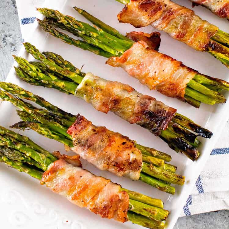 Overhead image of grilled bacon wrapped asparagus on white plate