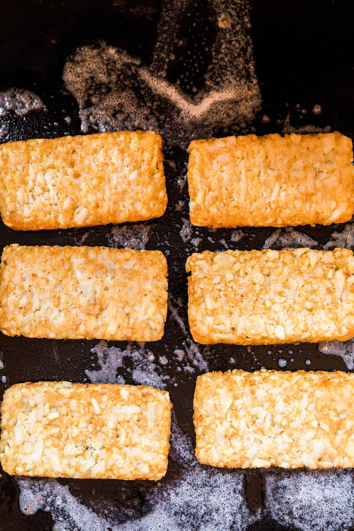 Placing frozen hash brown patties on Blackstone griddle for Breakfast Crunchwraps