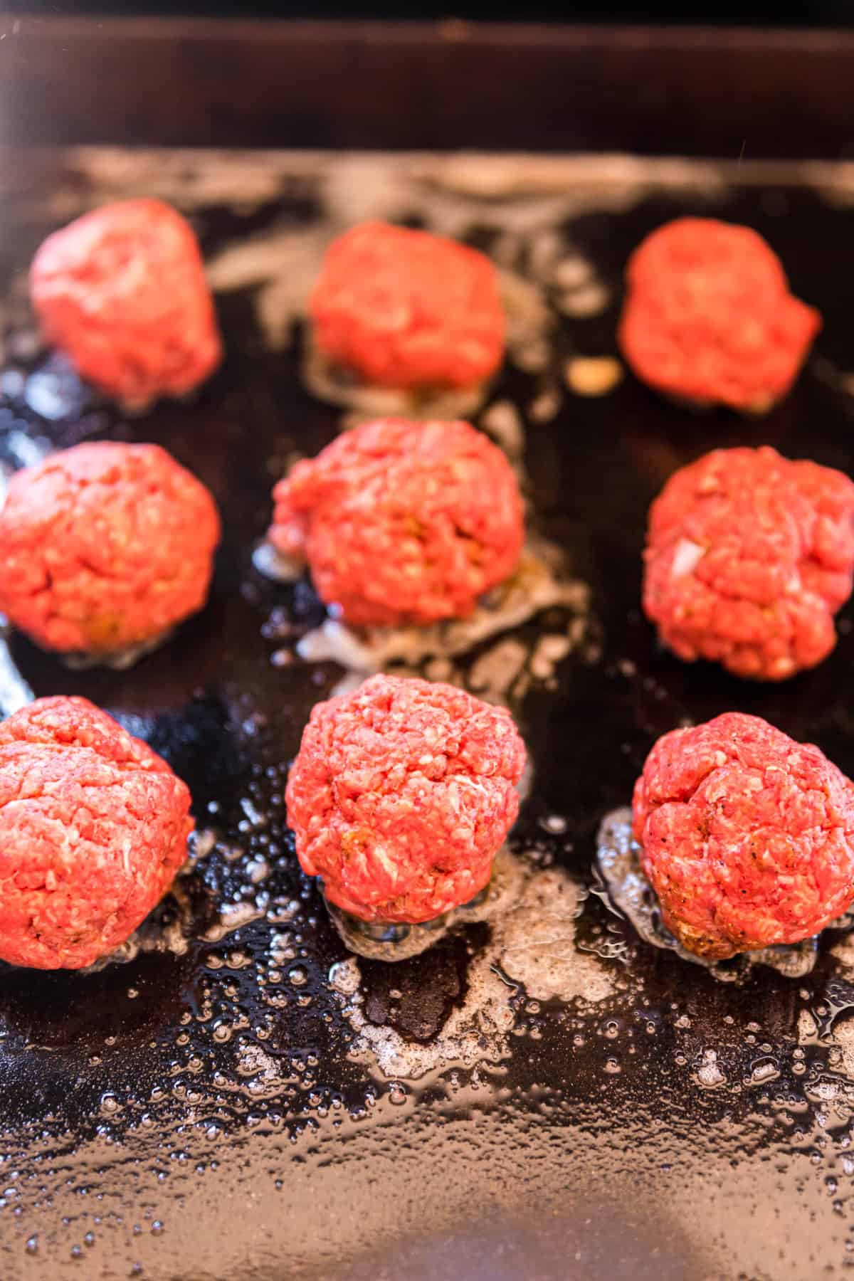 Placing meatballs on butter griddle for Blackstone Smash Burger Sliders