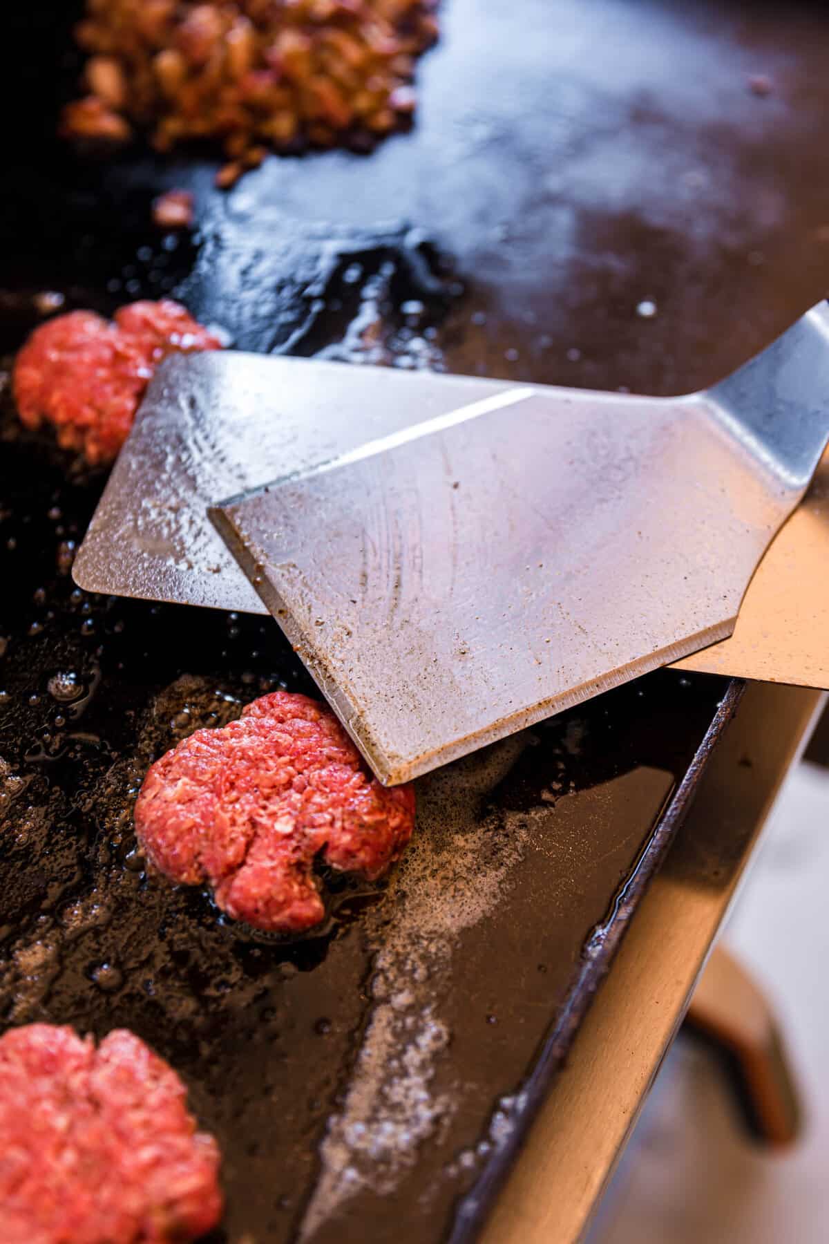 Smashing meatballs with flipper on buttered griddle for Blackstone Smash Burger Sliders