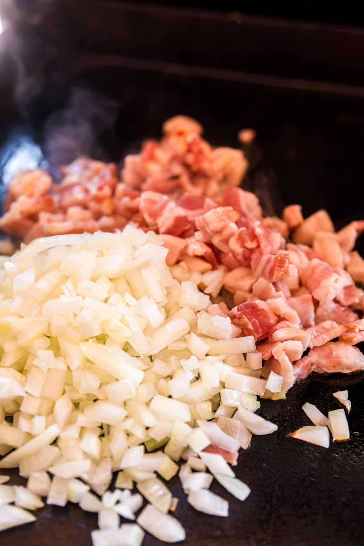 Tossing onion and bacon on Blackstone griddle for Slider Smash Burgers