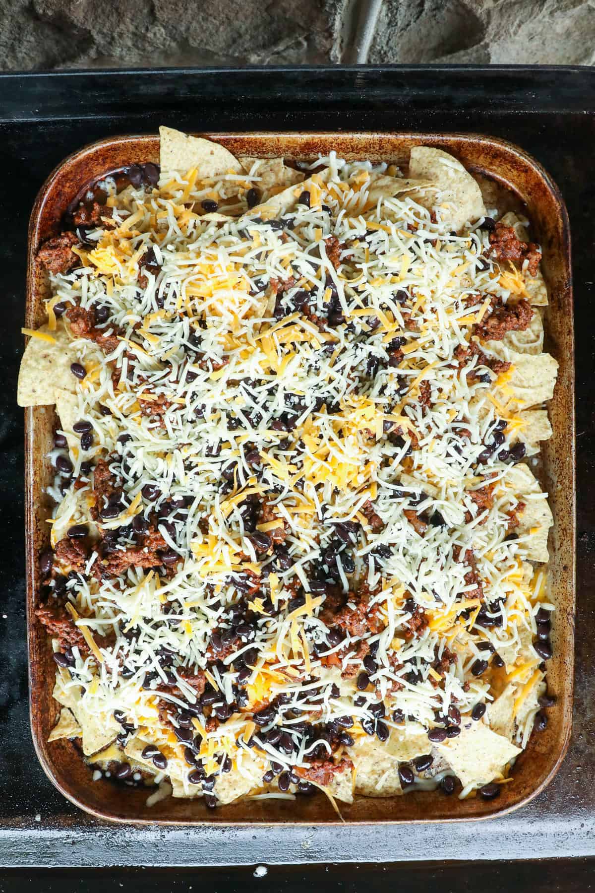 Topping layers with shredded cheese for Blackstone Nachos