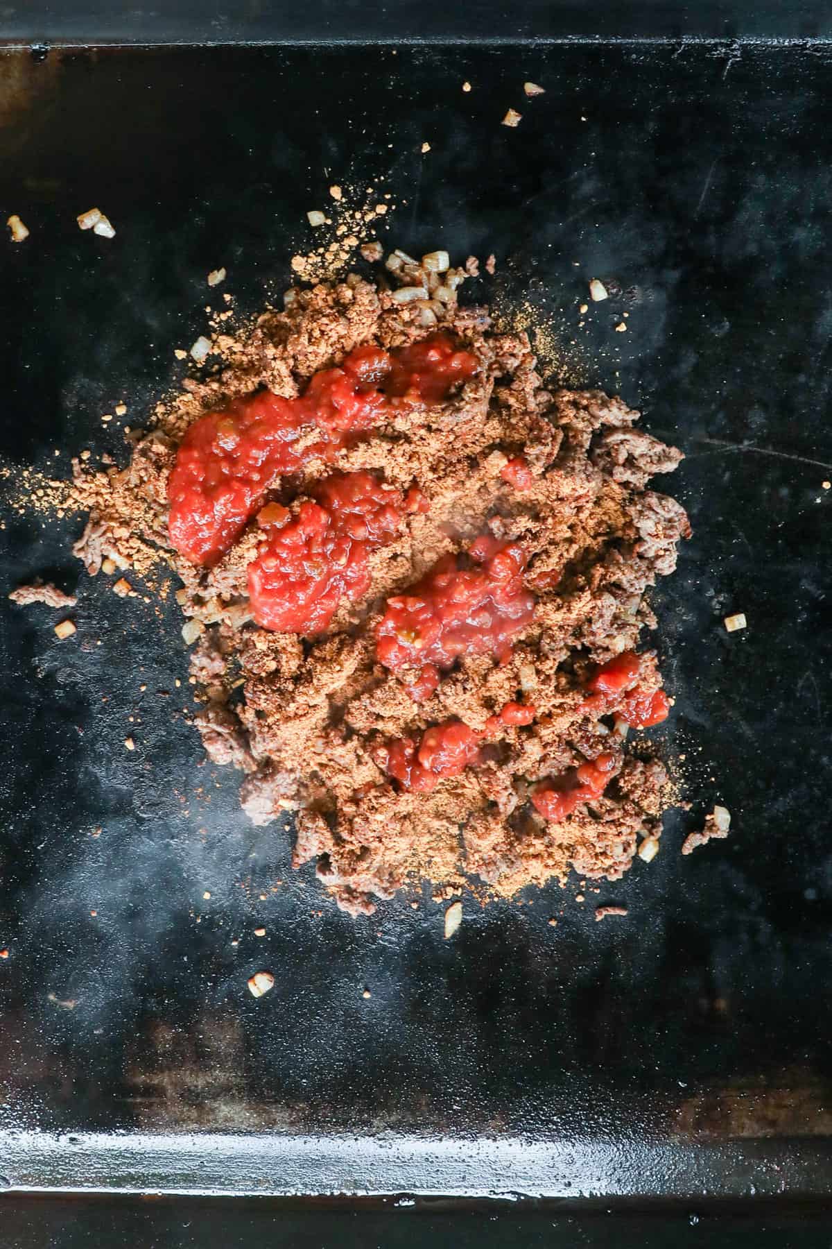 Adding salsa to browned and seasoned ground beef for Nachos on the Blackstone