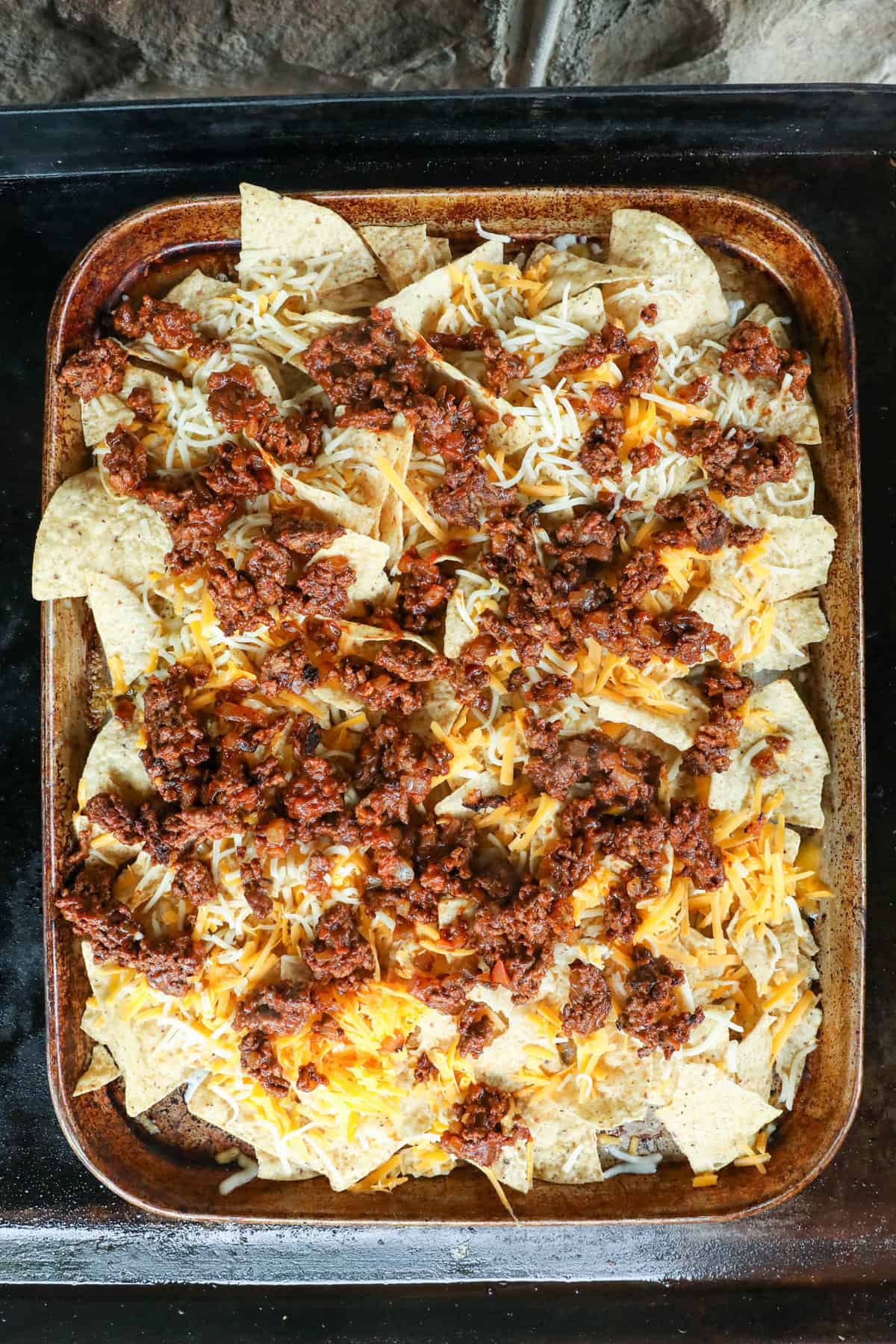 Adding seasoned ground beef to chips and cheese for Blackstone Nachos