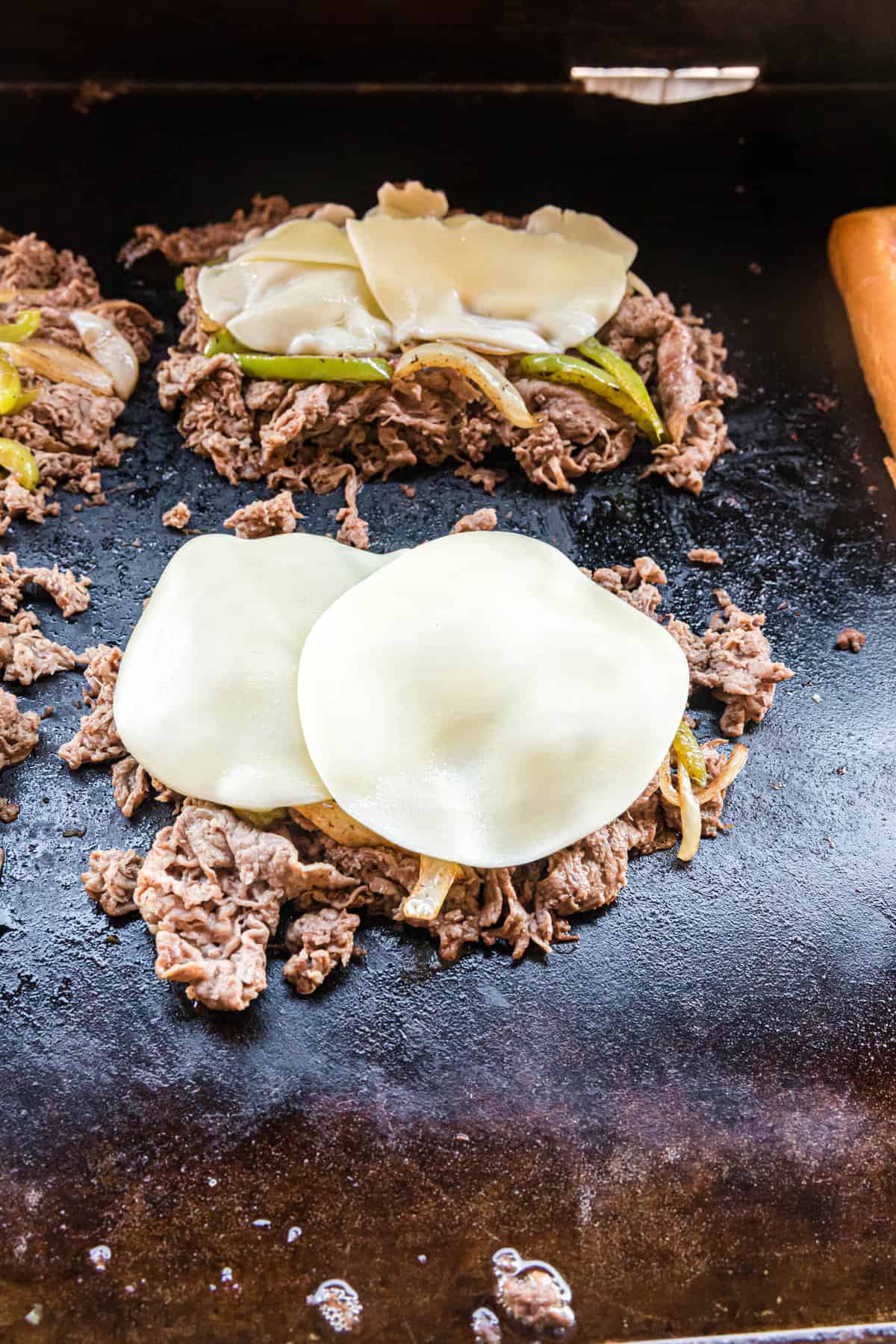 Topping steak and vegetables with provolone cheese for Philly Cheesesteak Blackstone recipe