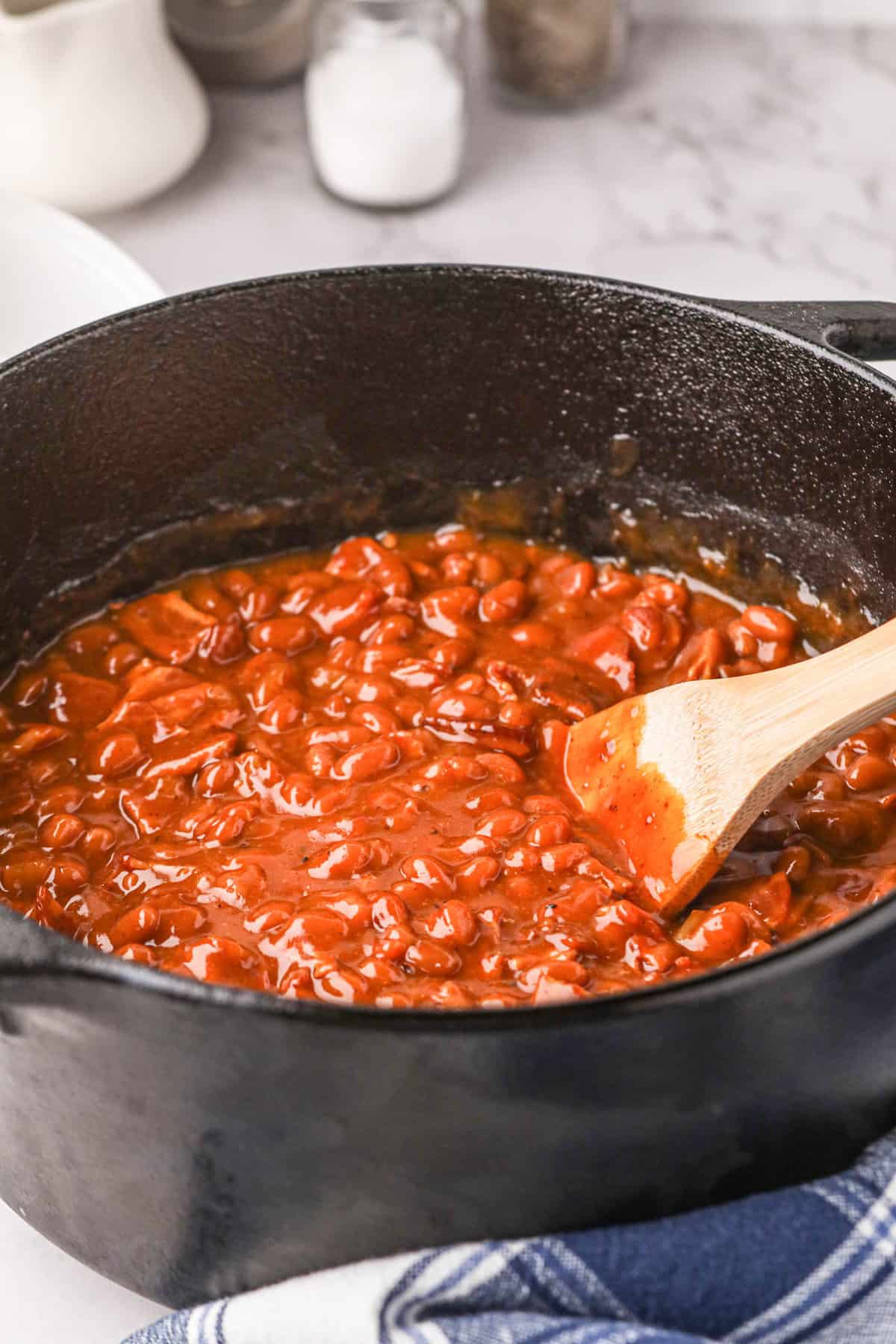 Stirring Smoked Baked Beans in dutch oven with a wooden spoon