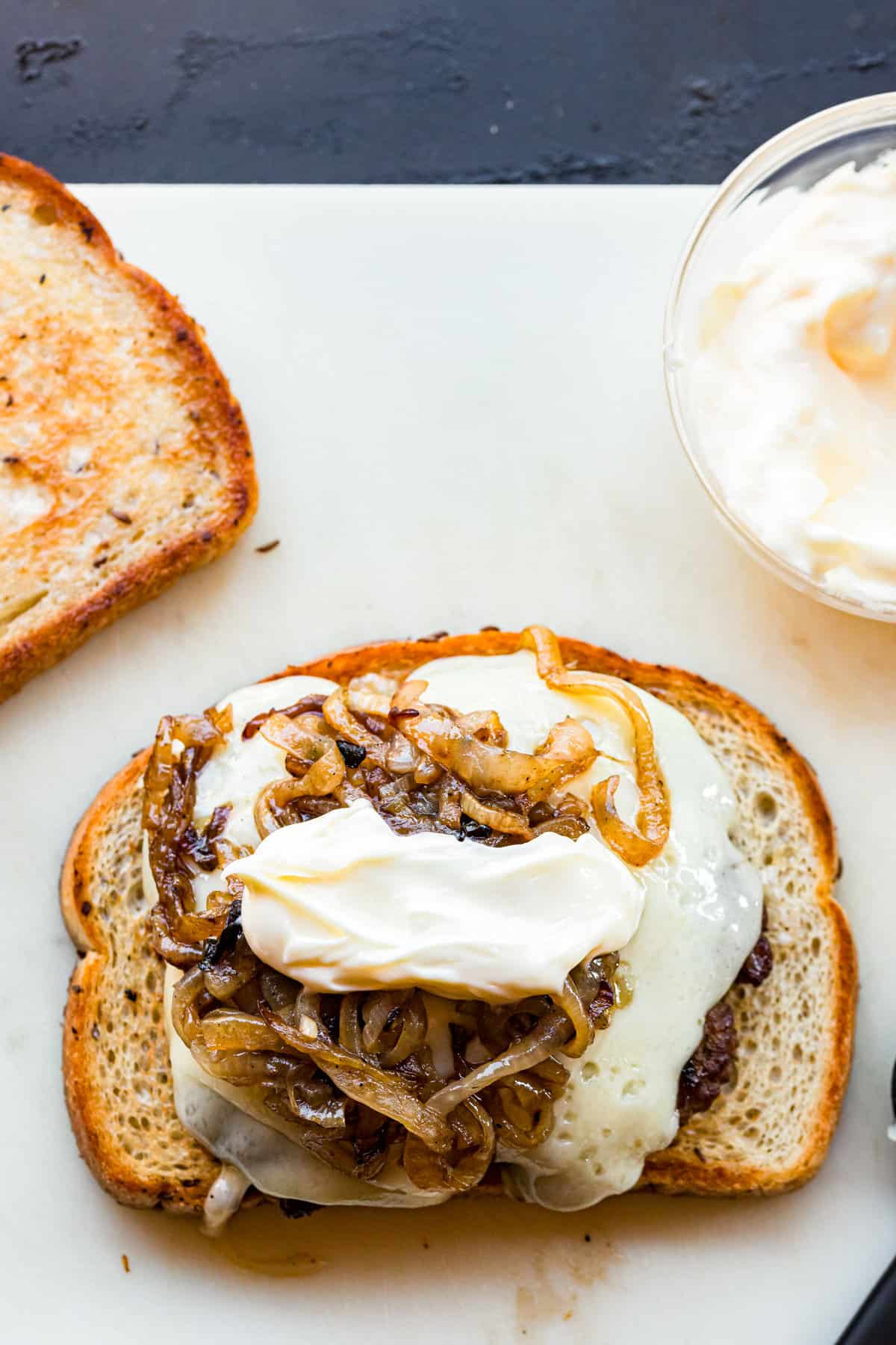 Adding patty melt ingredients to grilled bread for Blackstone Patty Melts