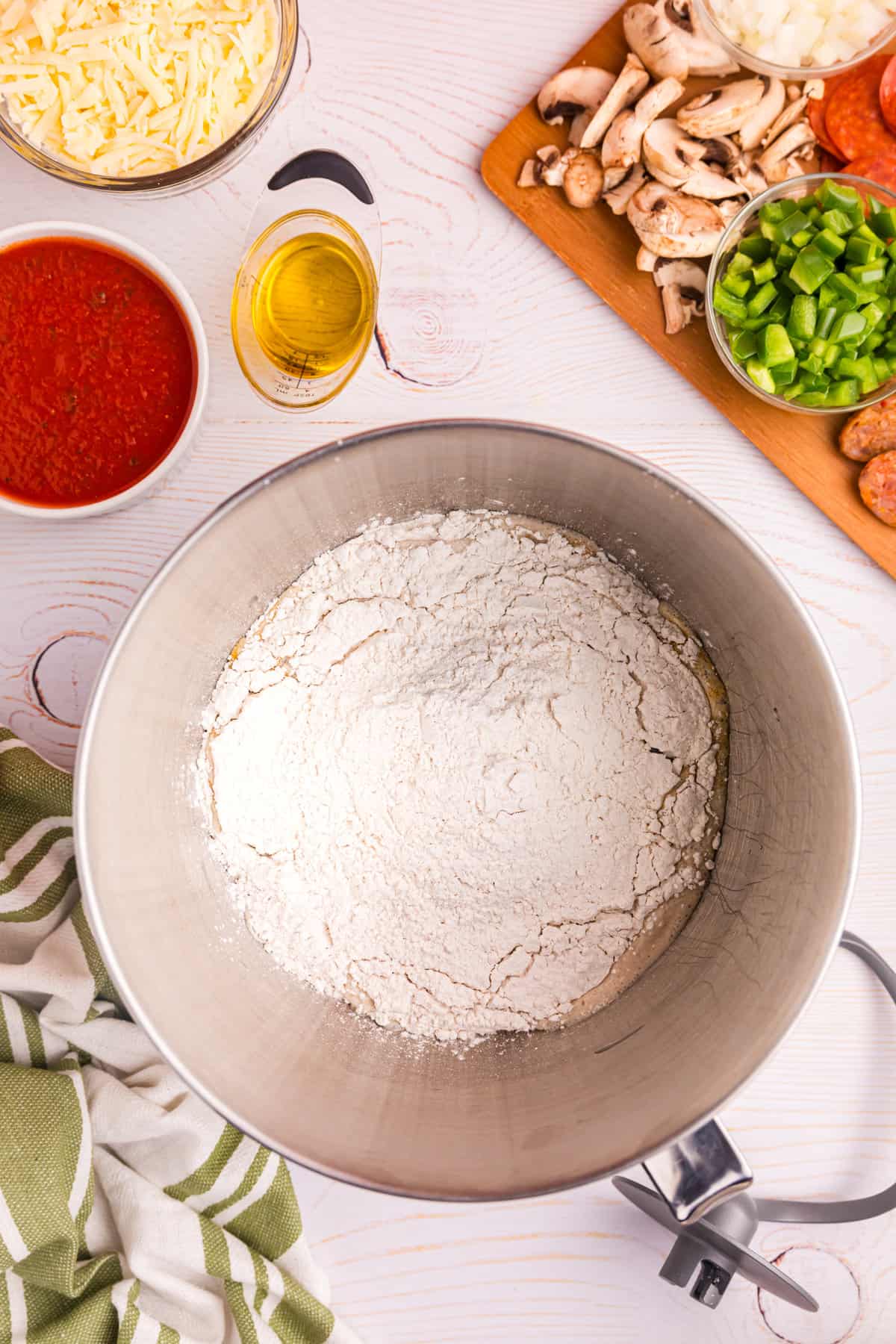 Adding flour to dough ingredients in mixing bowl for Blackstone Pizza recipe