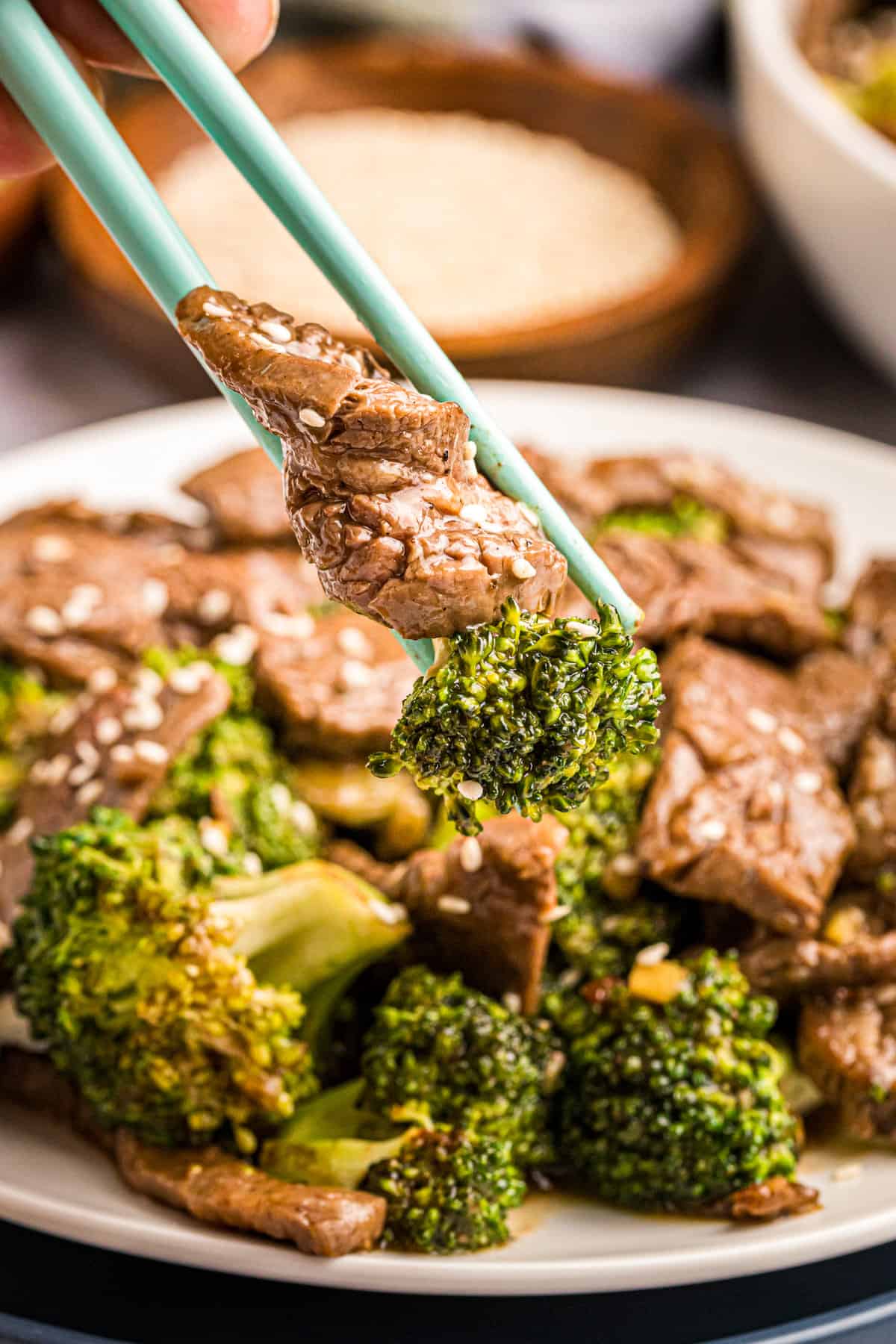 Blackstone Beef & Broccoli in shallow bowl using chopsticks to eat with