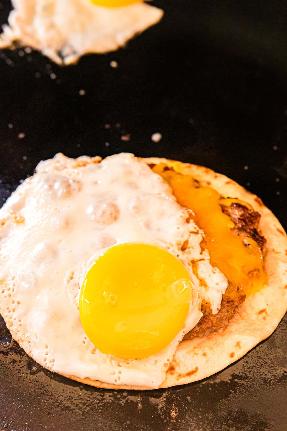 Adding fried egg on Smash Breakfast Taco recipe on Blackstone