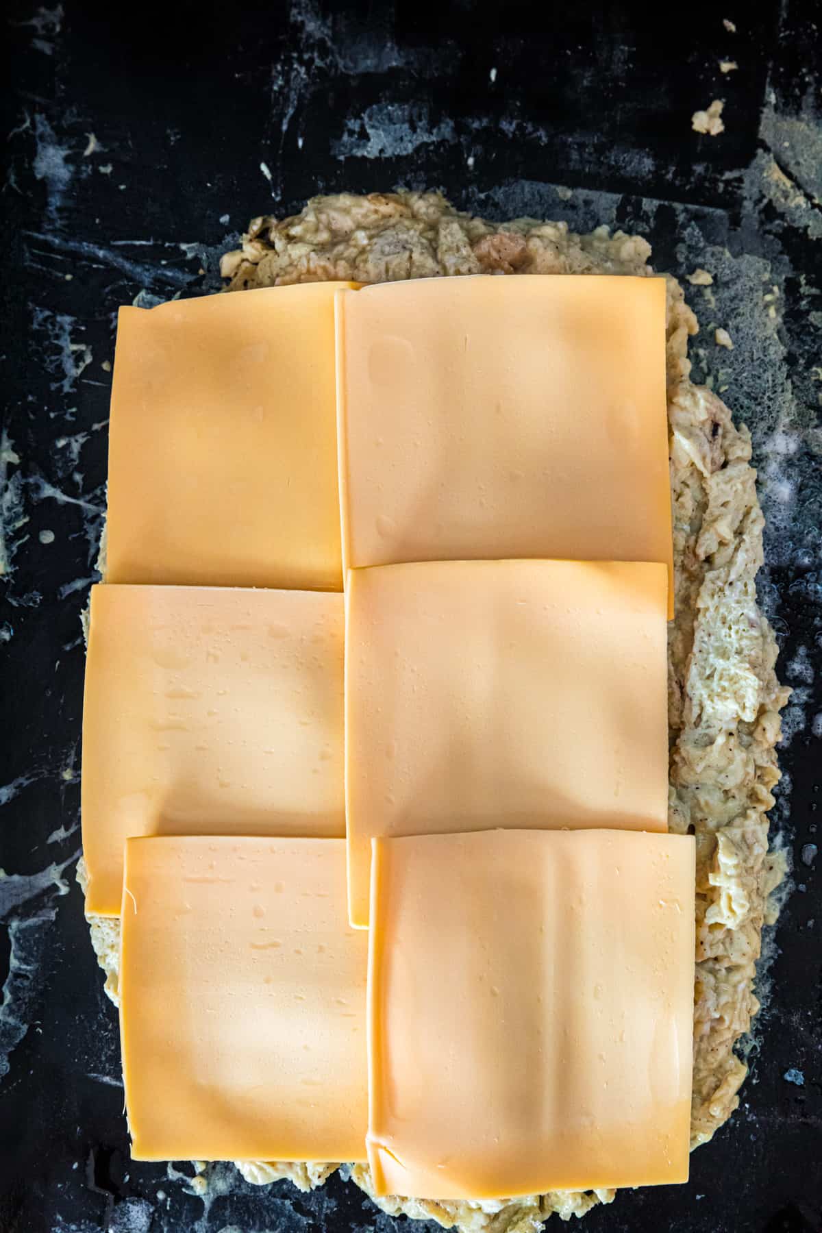 Adding sliced cheese to egg mixture on Blackstone for Blackstone Breakfast Sliders