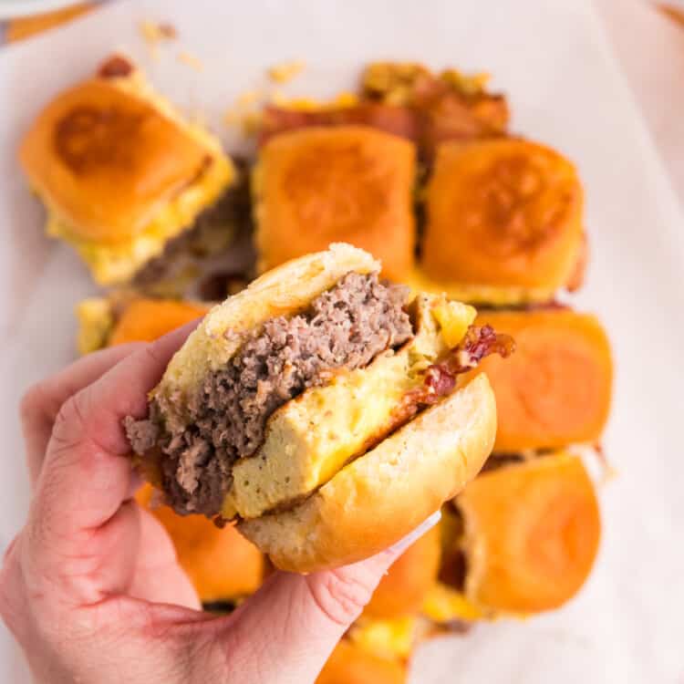 Blackstone Breakfast Sliders cut apart on serving plate and grabbing one in hand to try the first bite