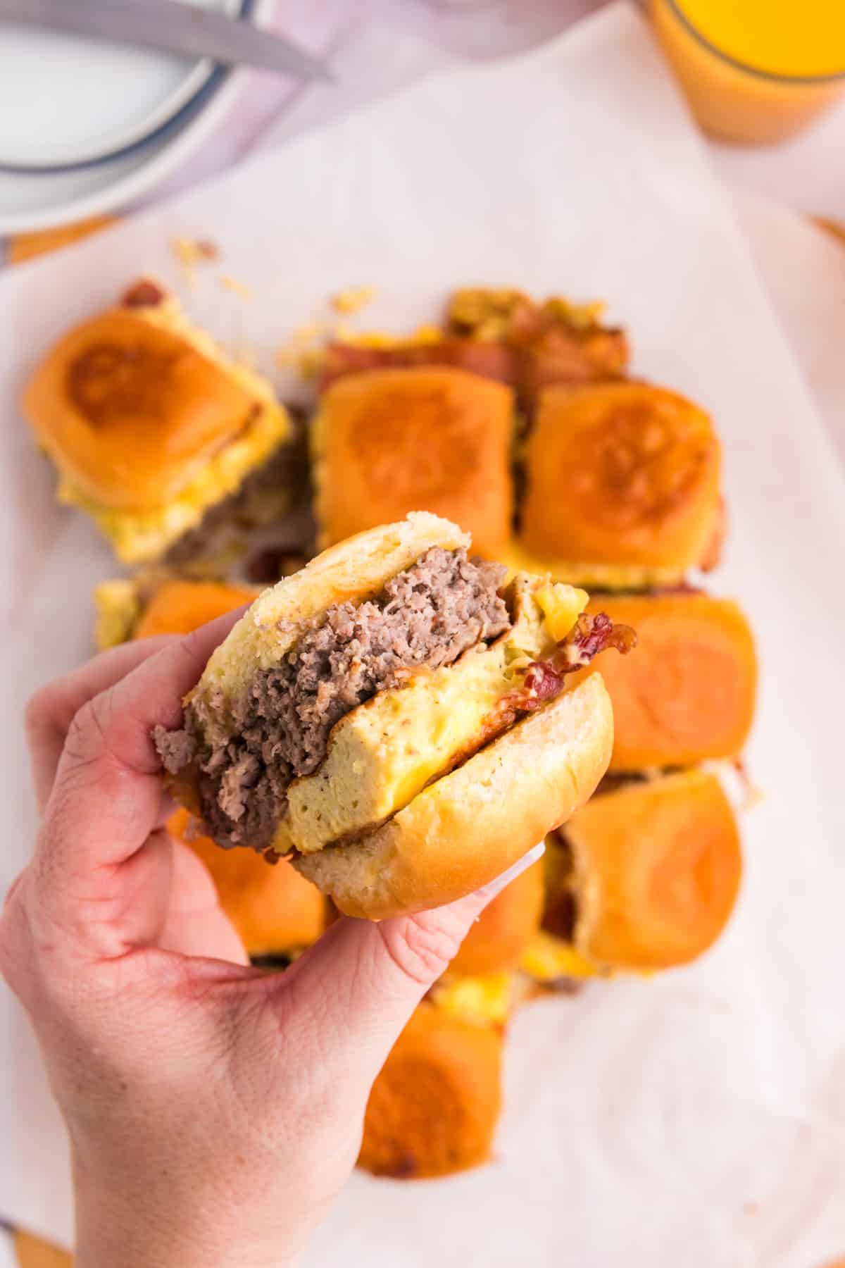 Blackstone Breakfast Sliders cut apart on serving plate and grabbing one in hand to try the first bite