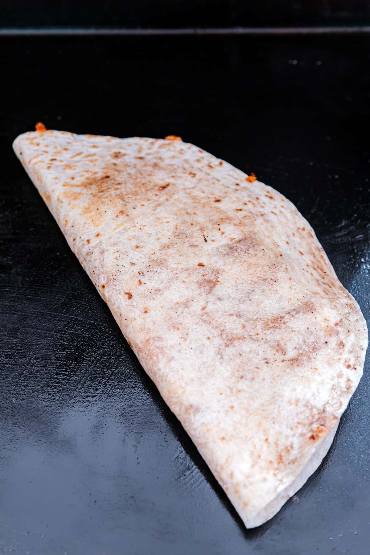 Folding burrito sized torilla in half while still on the griddle for Blackstone Chicken Quesadilla