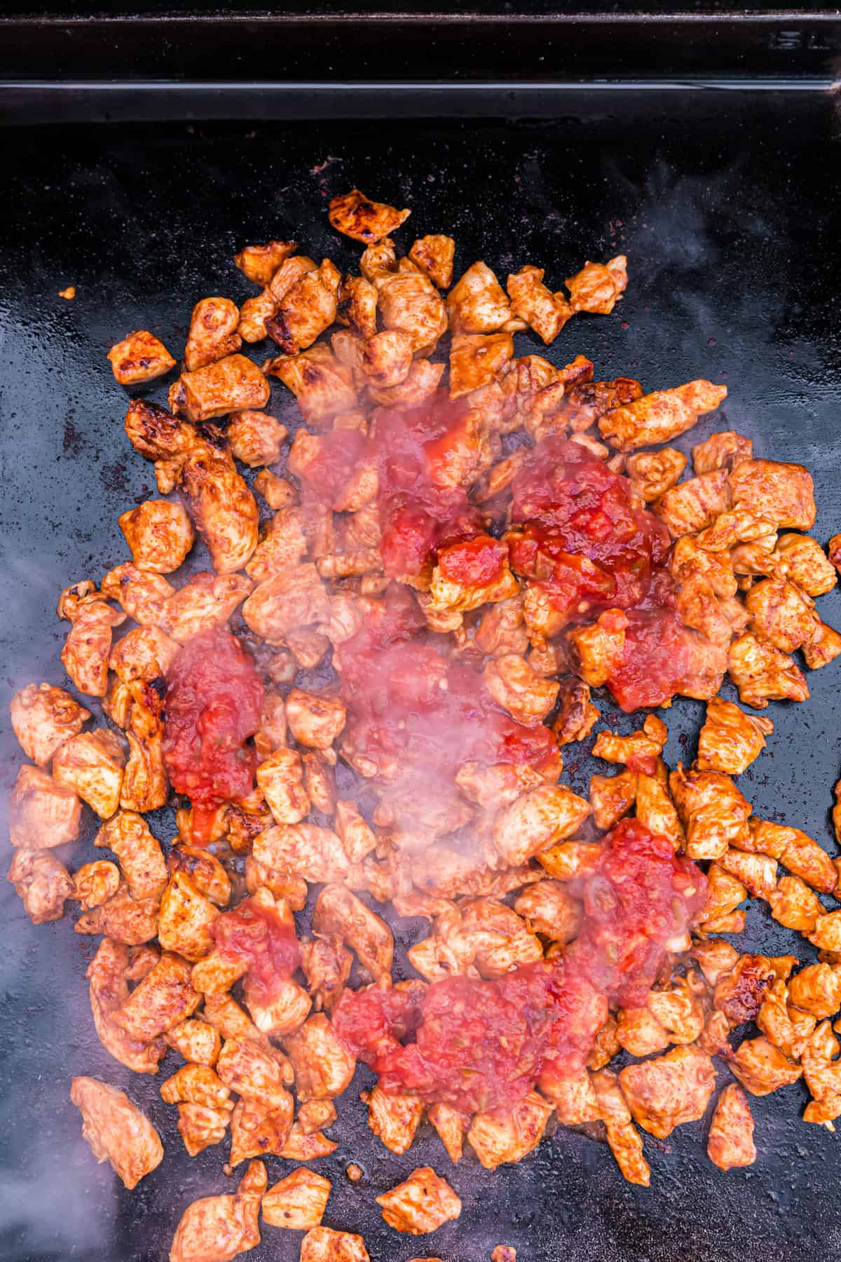 Adding salsa to cooked chicken chunks on griddle for Blackstone Chicken Quesadilla