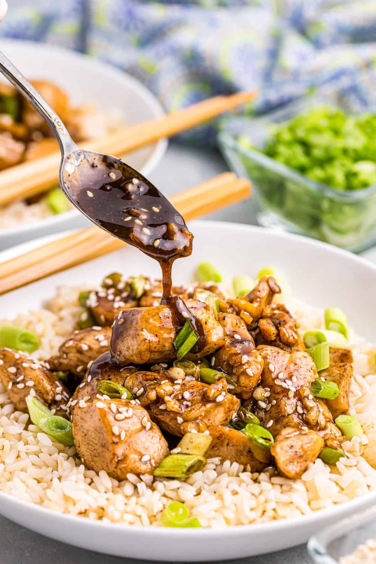 Blackstone Teriyaki Chicken over a bed of rice with spoong drizzling soy sauce and seasame seeds