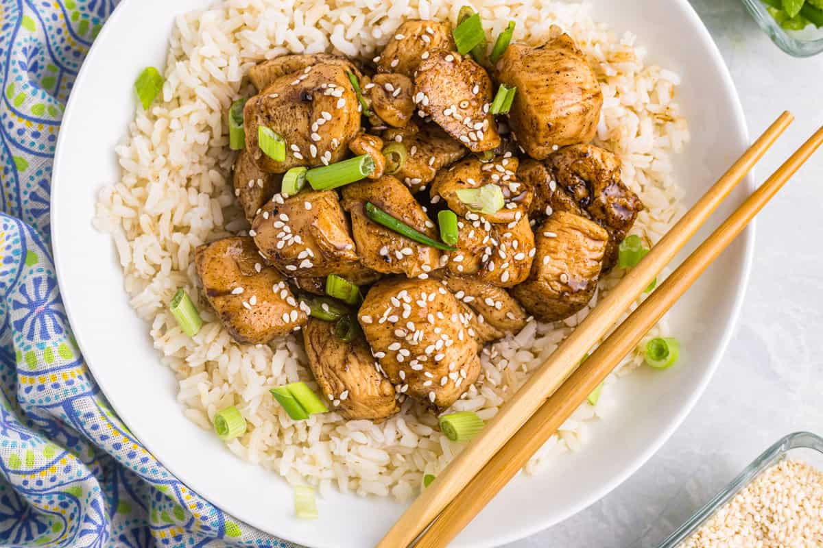 Teriyaki Chicken atop of a bed of rice in shallow bowl with chopsticks
