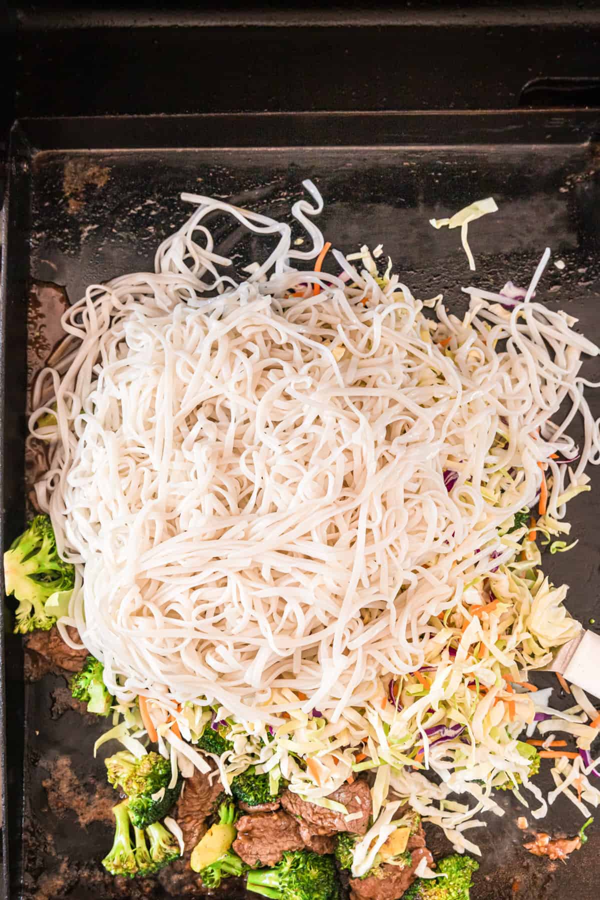 Adding cooked rice noodles and coleslaw to Blackstone Beef Stir Fry recipe