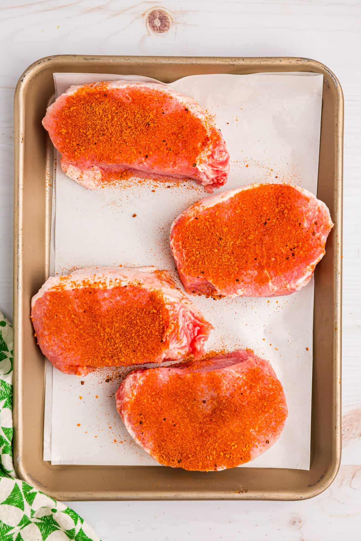 Seasoned pork chops with Gimme Some Grilling Pork Seasoning on parchment lined baking sheet for Blackstone Pork Chops Recipe