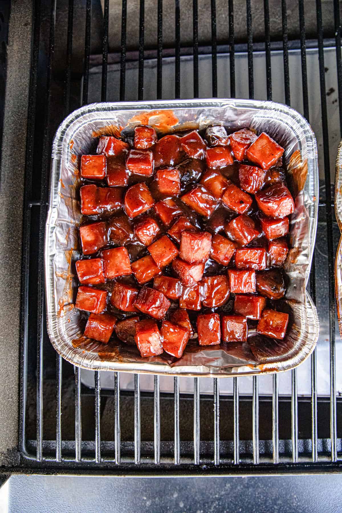 Spam Burnt Ends lathered in BBQ sauce in square tin on smoker