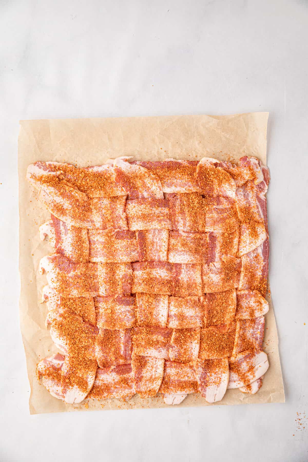 Adding seasoning to bacon weave for Bacon Explosion recipe