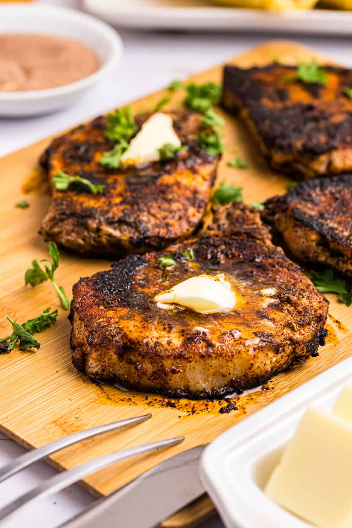 Blackstone Blackened Pork Chops hot off the griddle on wooden cutting board topped with dollops of butter