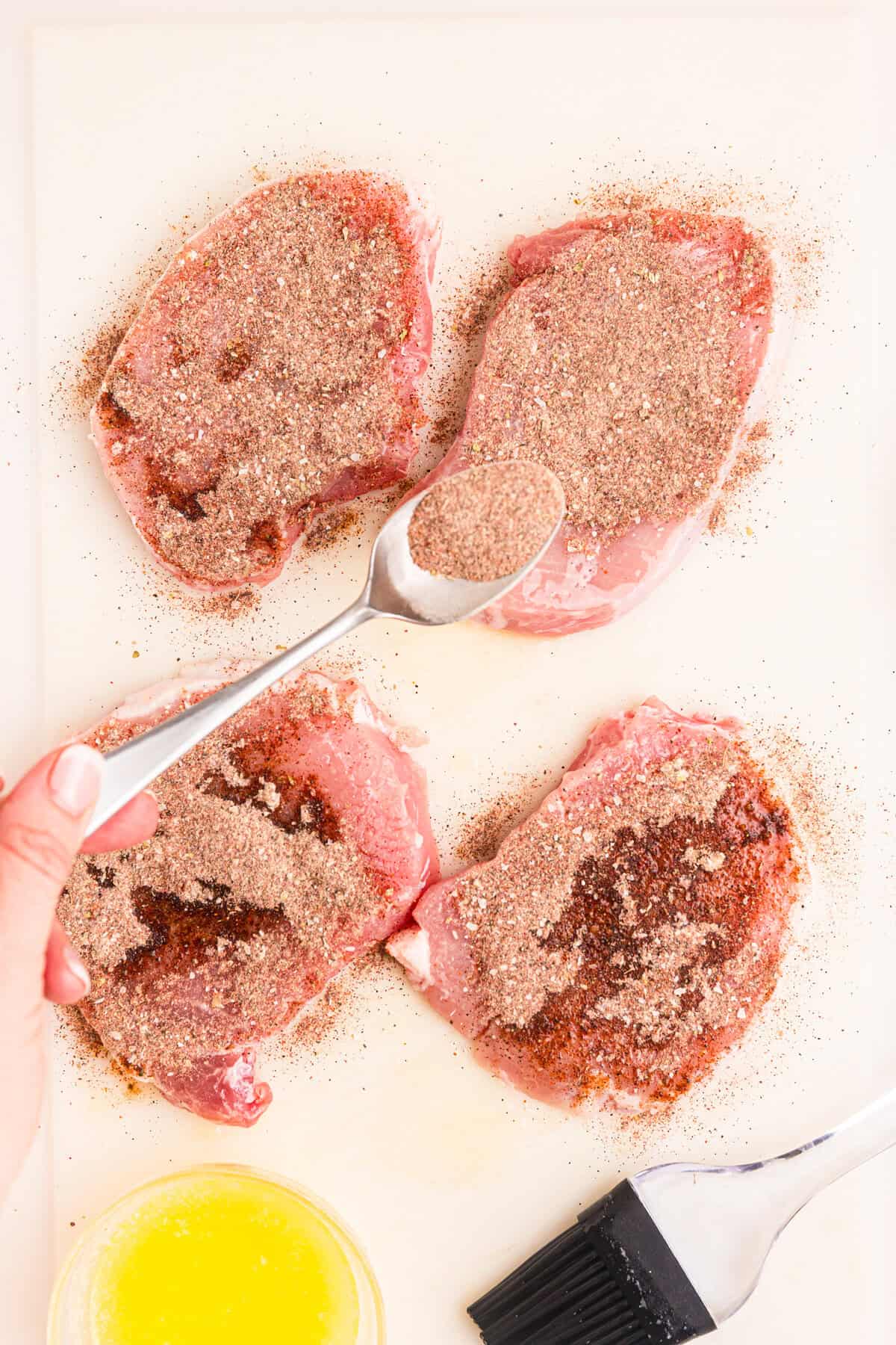 Generously coating buttered pork chops with seasoning for  Blackstone Blackened Pork Chops