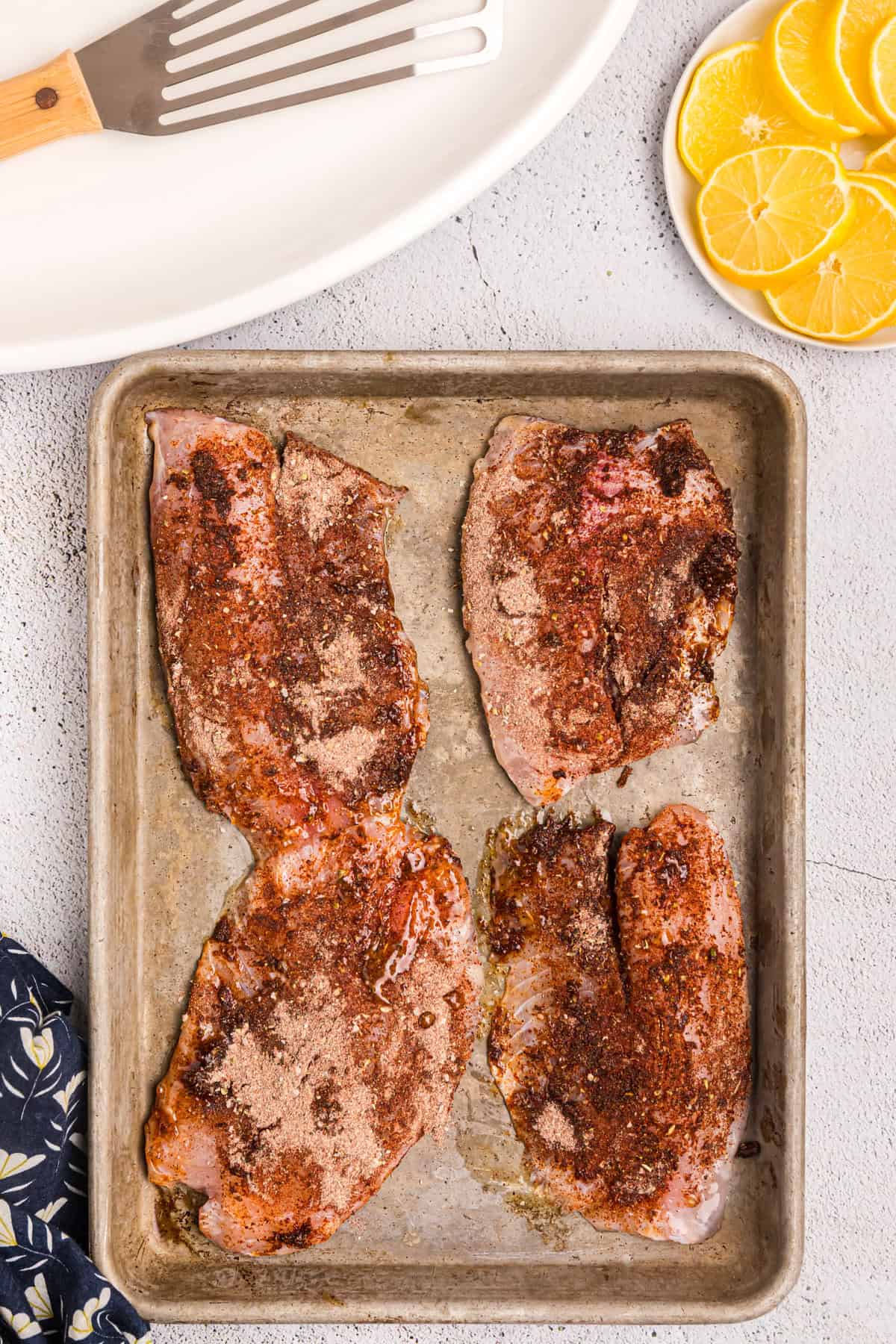 Buttered and seasoned fish fillets on a cooking sheet before moving to the Blackstone for Blackened Fish recipe