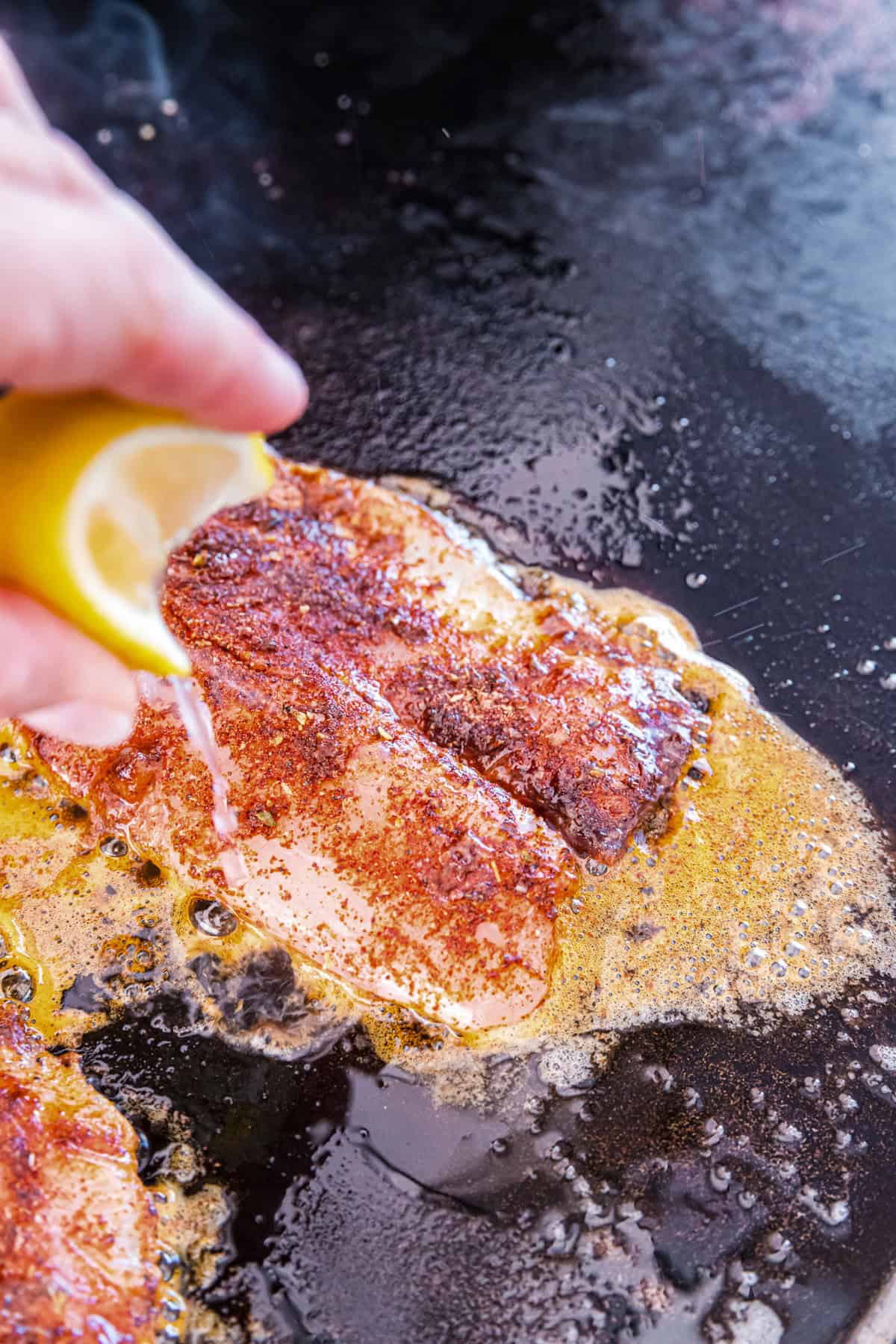 Squeezing lemon juice from fresh lemon slice over seasoned fish fillets for Blackstone Blackened Fish 