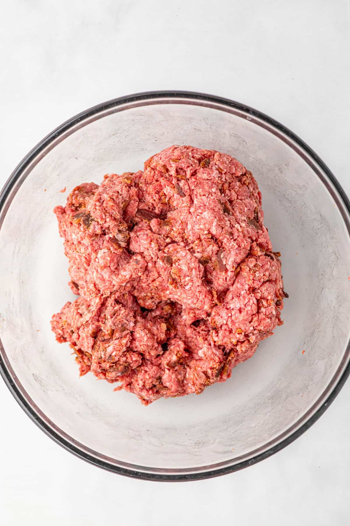 Ground beef, bacon bits, and seasonings in glass mixing bowl for Bacon Cheese Stuffed Burgers recipe