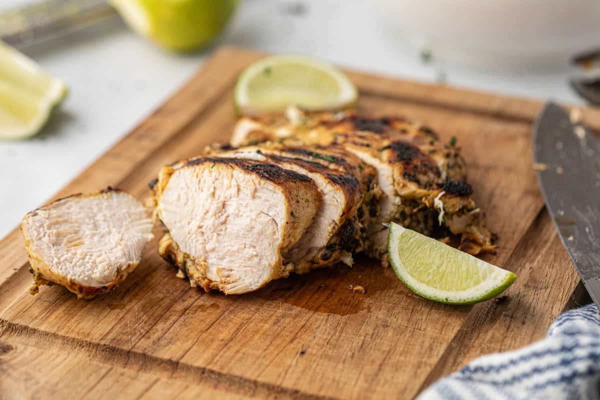 Grilled Cilantro Lime Chicken sliced with fresh limes on wooden cutting board