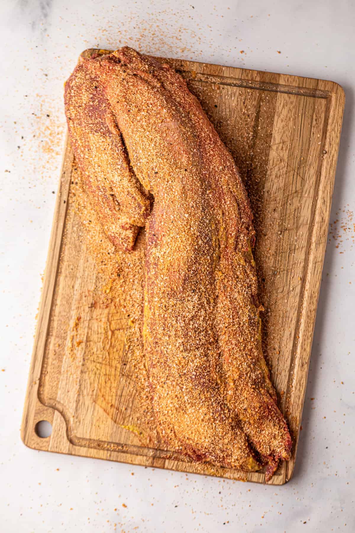 Smoked Beef Tenderloin on cutting board prior to smoking smothered in yellow mustard and beef rub