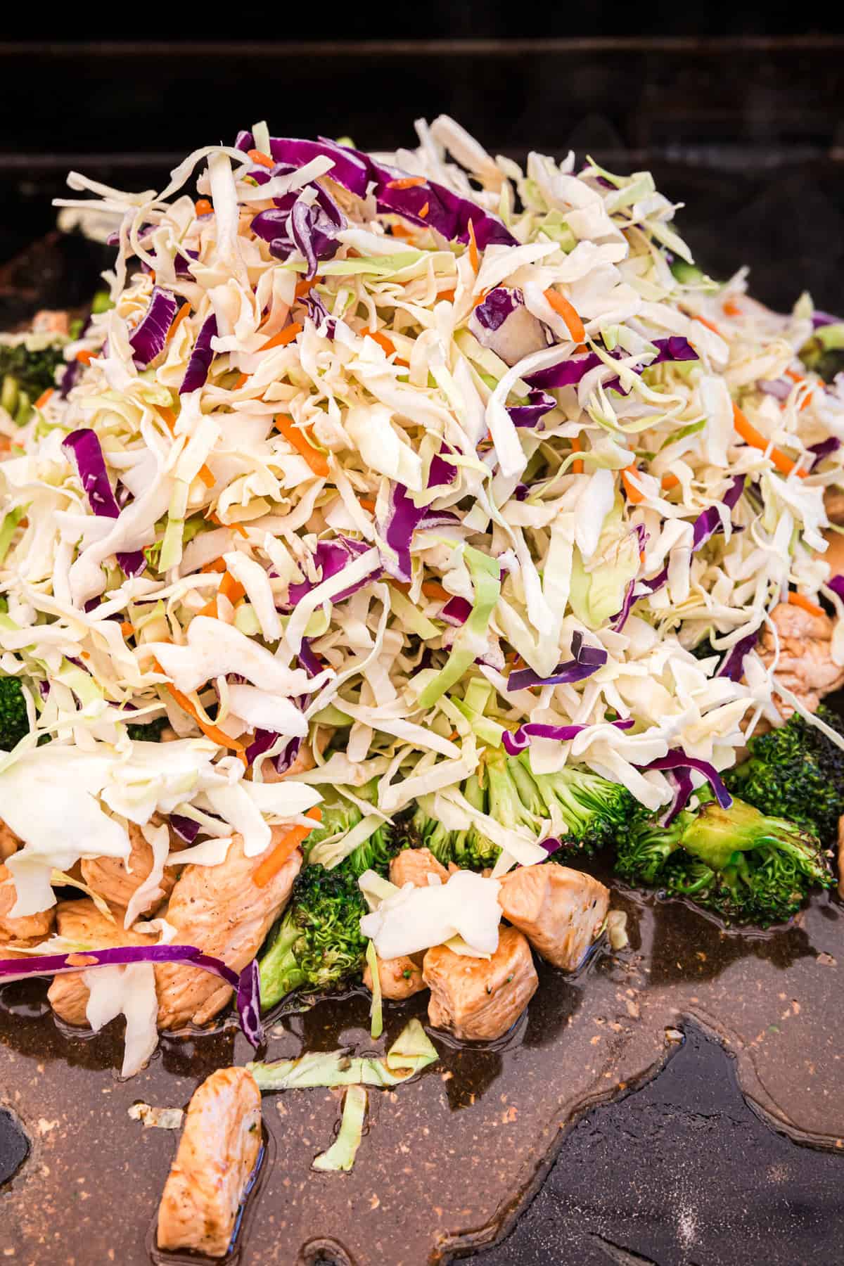 Adding mixed cole slaw to ingredients on the griddle for Blackstone Chicken Stir Fry recipe