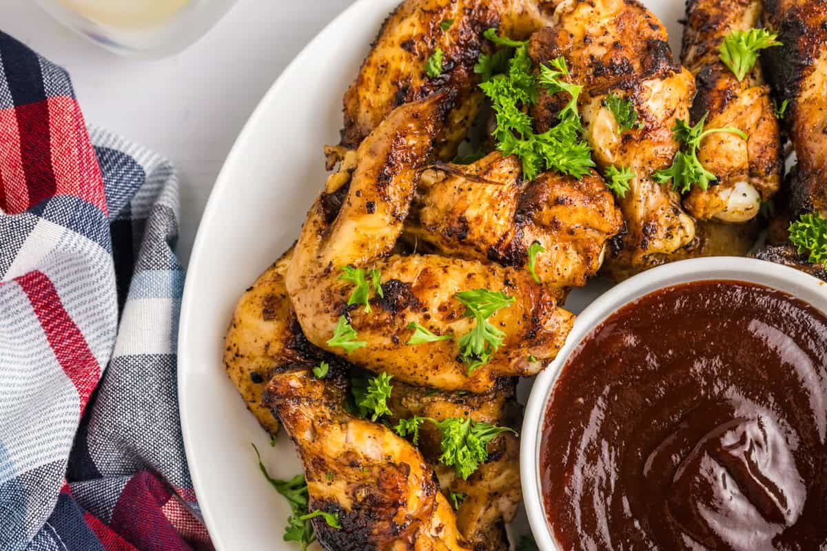 Blackstone Chicken Wings arranged on serving plate with BBQ dipping sauce in small bowl