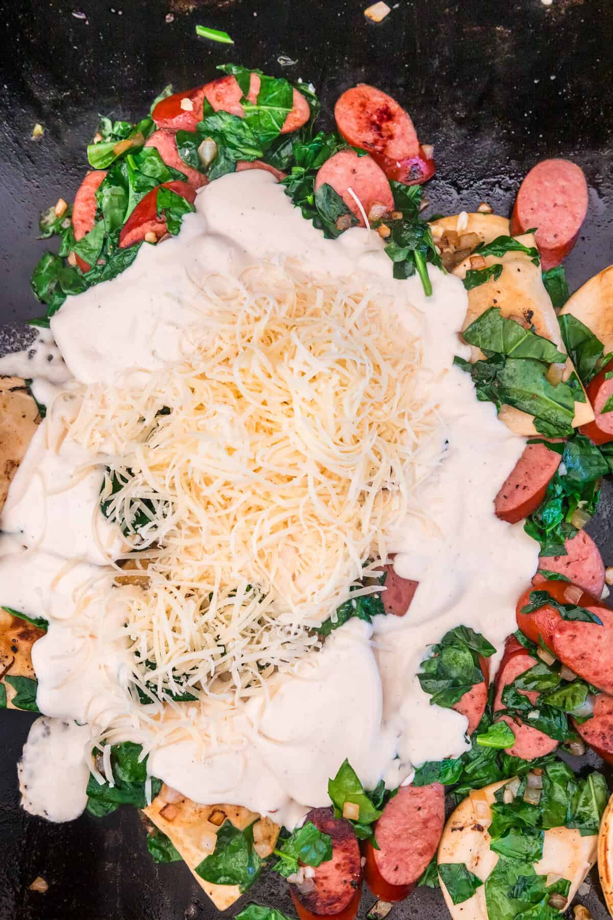 Alfredo sauce and Parmesan cheese added over Blackstone Sausage and Pierogies mixture on the griddle