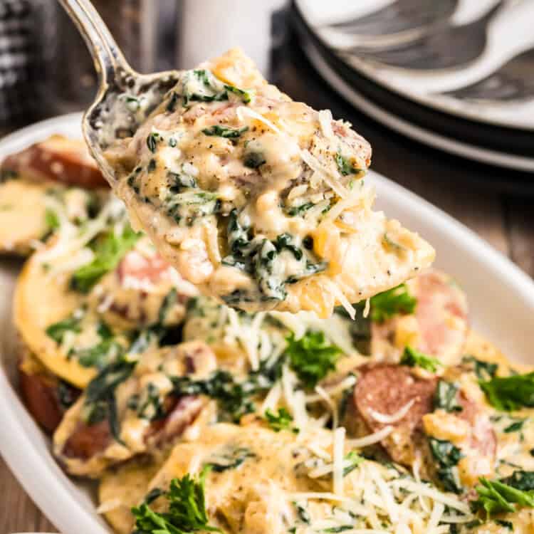Blackstone Sausage and Pierogies in shallow white serving dish with a serving spoon lifting the first bite