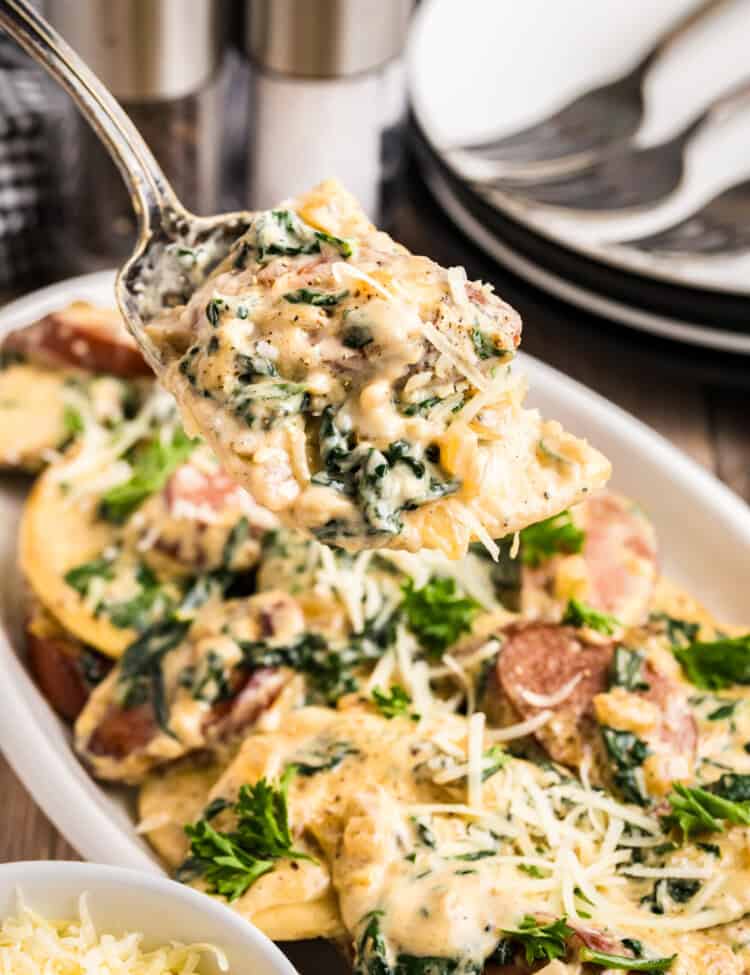 Blackstone Sausage and Pierogies in shallow white serving dish with a serving spoon lifting the first bite