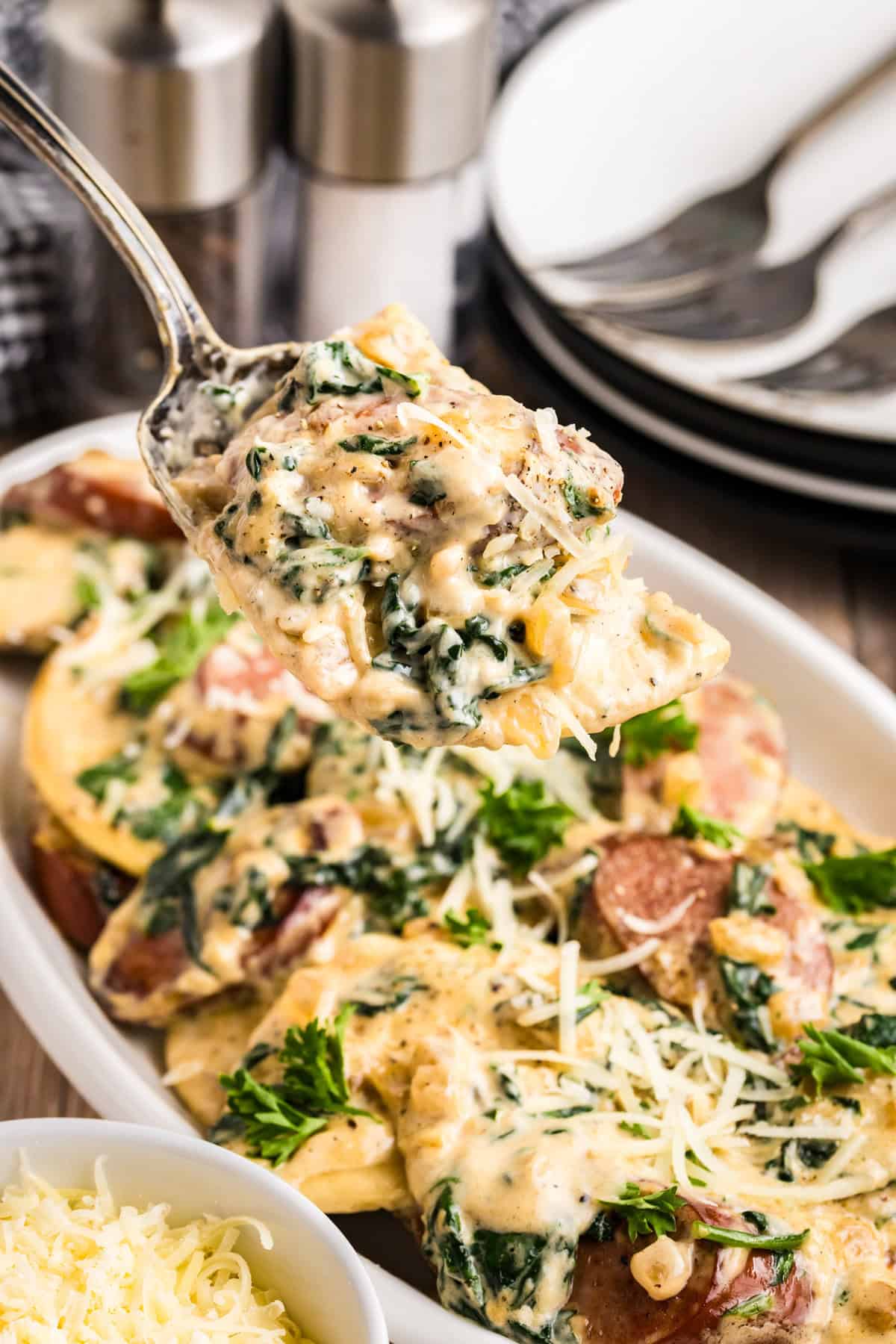 Blackstone Sausage and Pierogies in shallow white serving dish with a serving spoon lifting the first bite