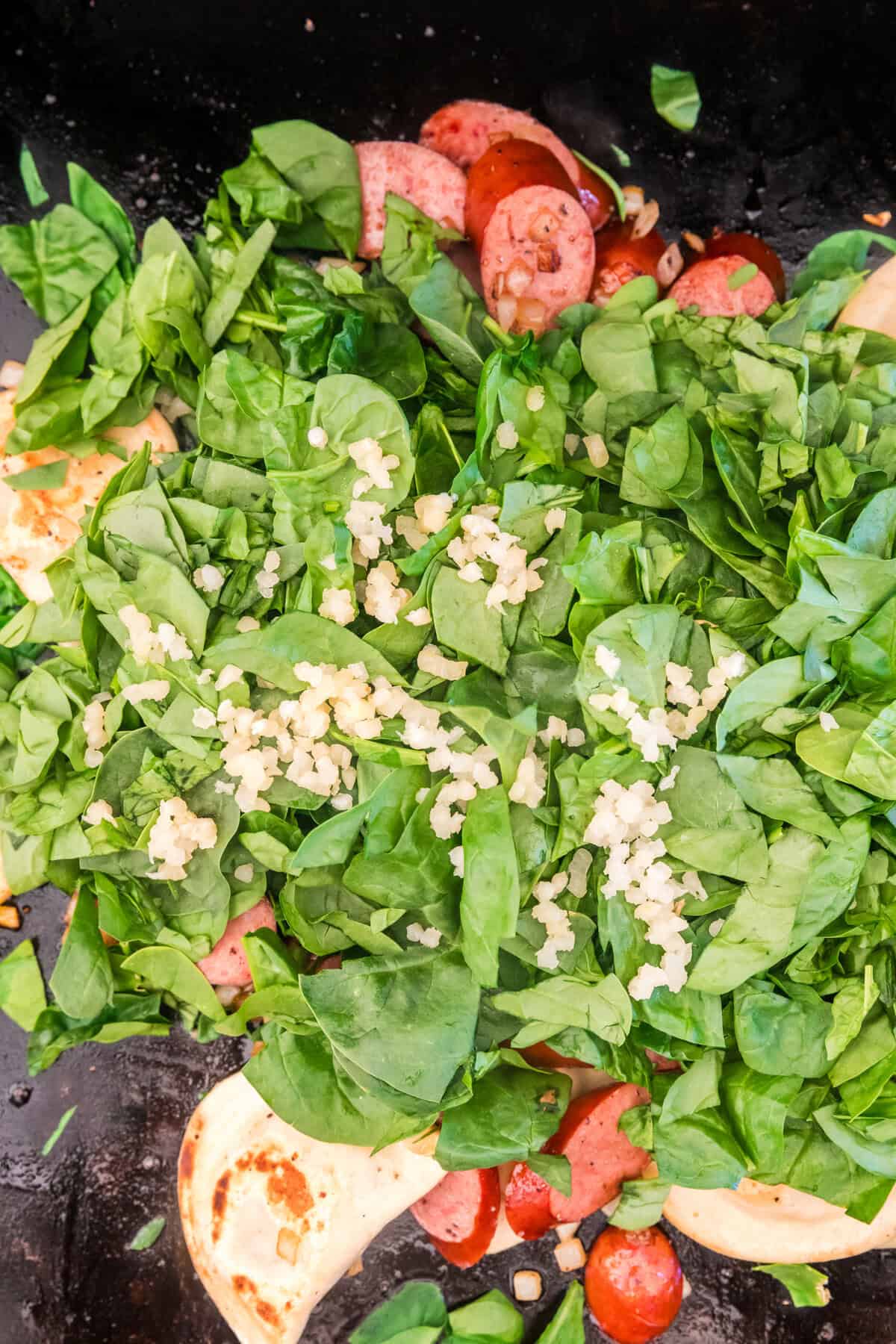 Adding spinach and minced garlic to Blackstone Sausage and Pierogies mixture