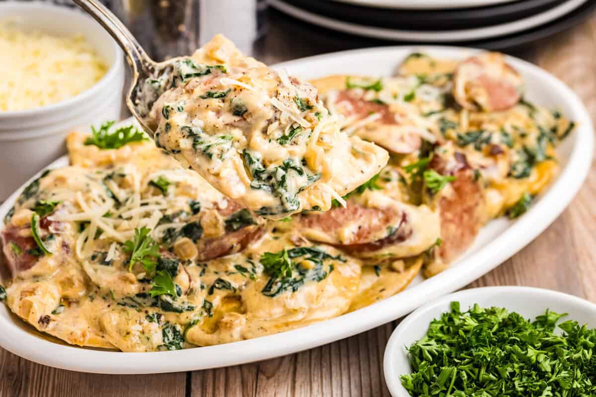 Blackstone Sausage and Pierogies in shallow white serving dish with a serving spoon lifting the first bite