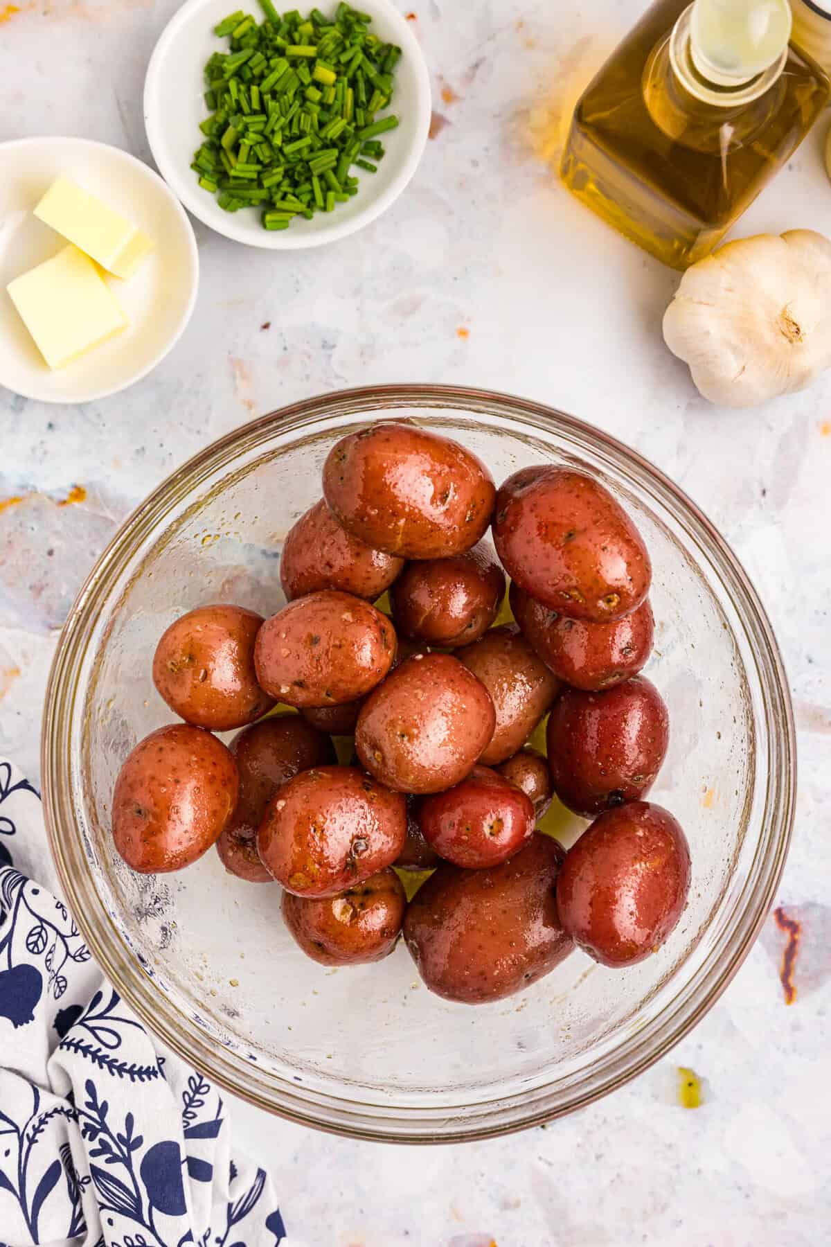 Coating the boiled baby potatoes with seasoning mixture in large glass bowl before smashing on the Blackstone for Blackstone Smashed Potatoes recipe