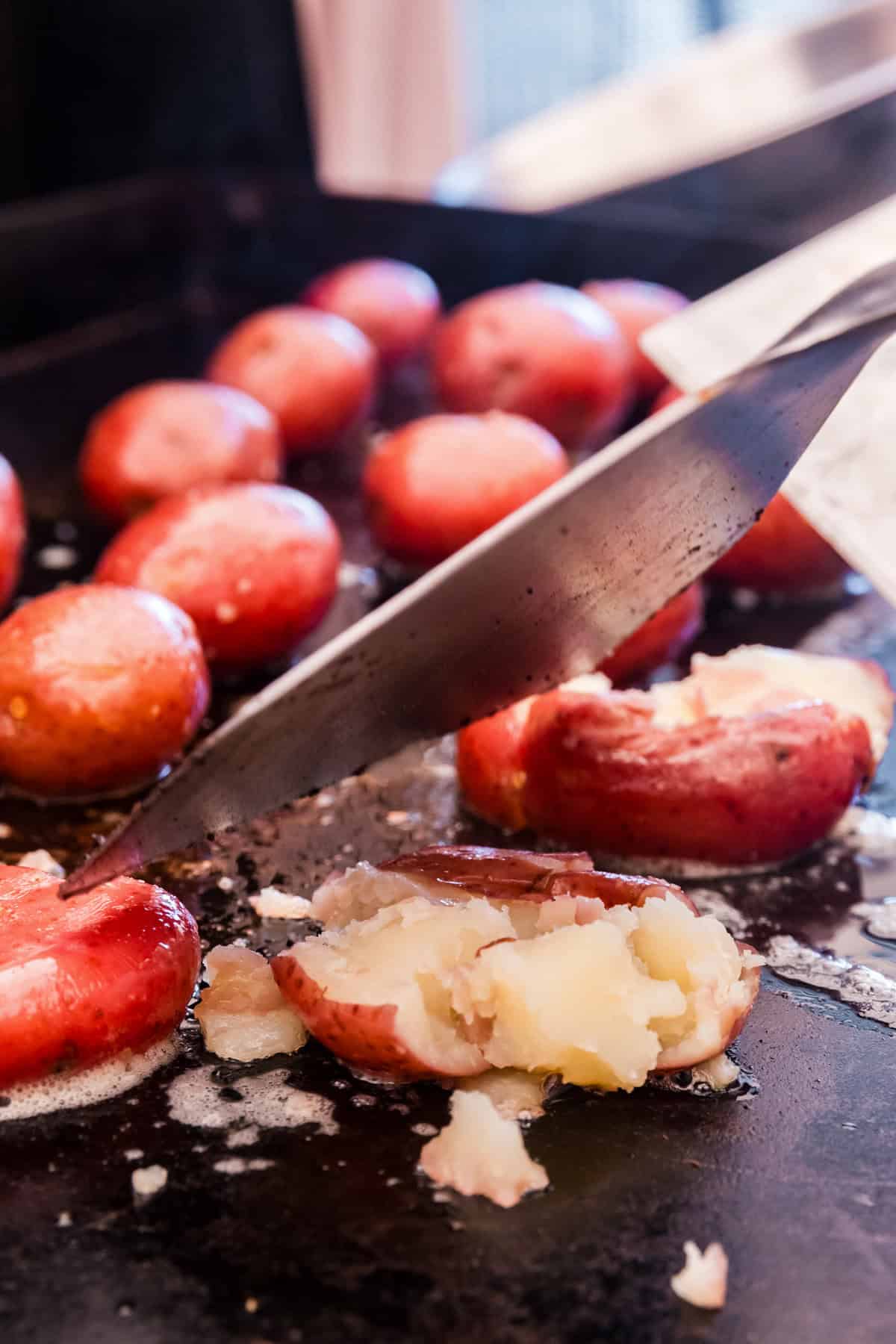 Using grill spatula to smash the potatoes on the griddle for Blackstone Smashed Potatoes